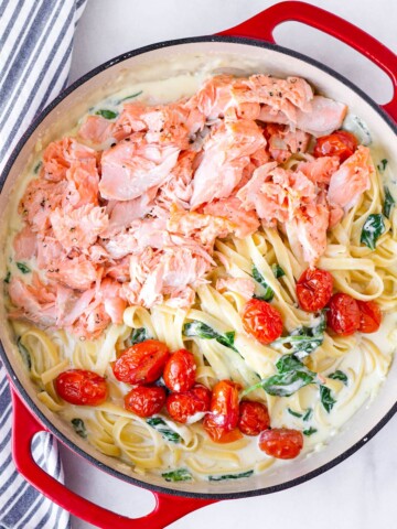 creamy salmon fettuccine with creamy sauce, tomatoes, and spinach in a red dutch oven