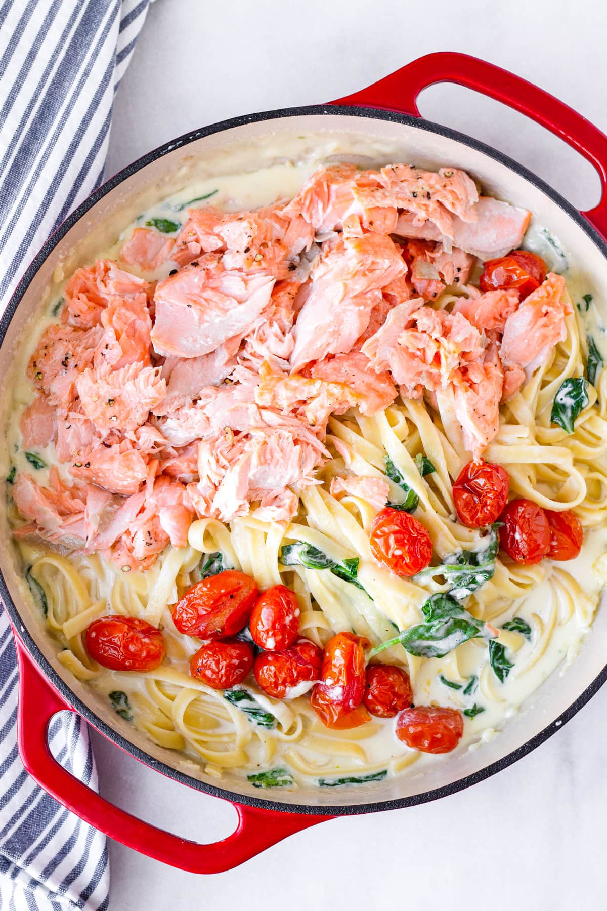 creamy salmon fettuccine with creamy sauce, tomatoes, and spinach in a red dutch oven