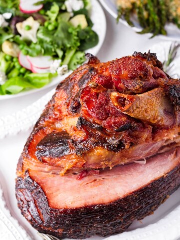 a whole roasted Easter glazed ham with salad side dishes in the back