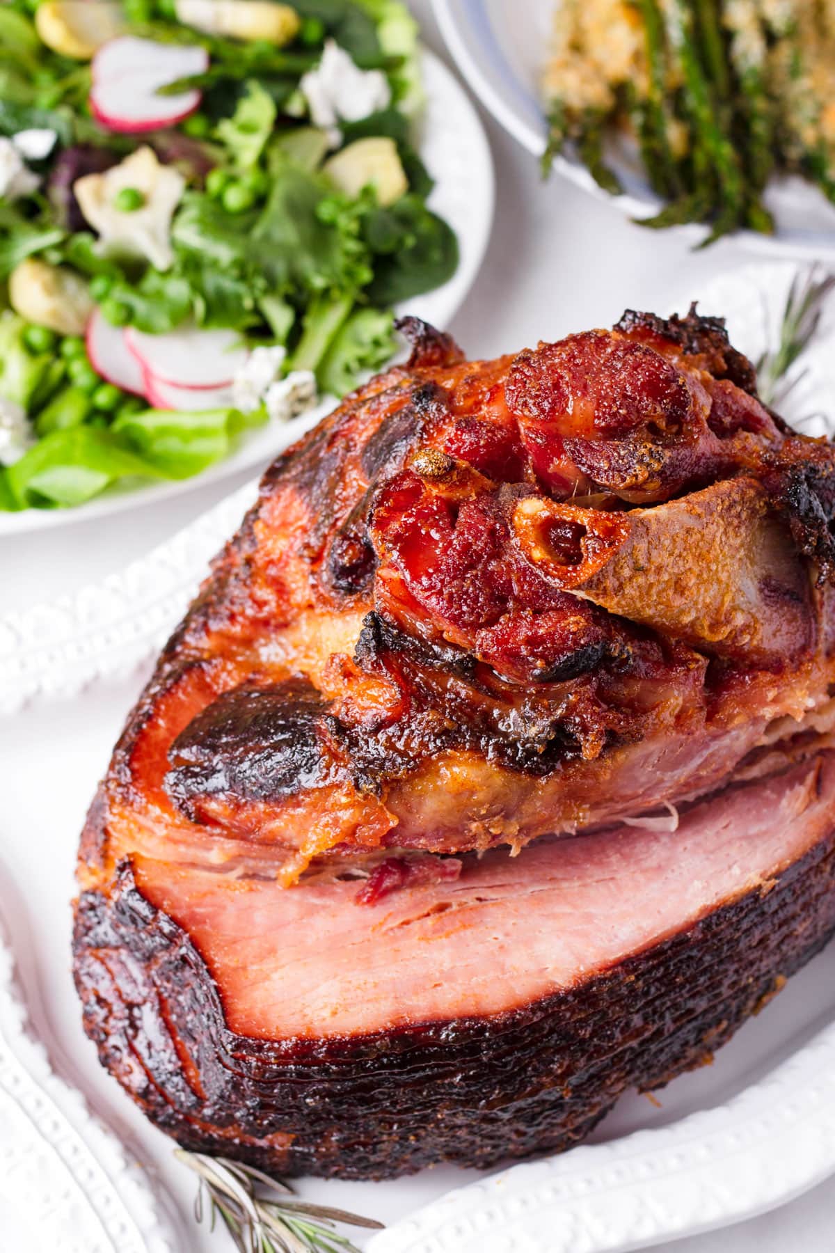 a whole roasted Easter glazed ham with salad side dishes in the back