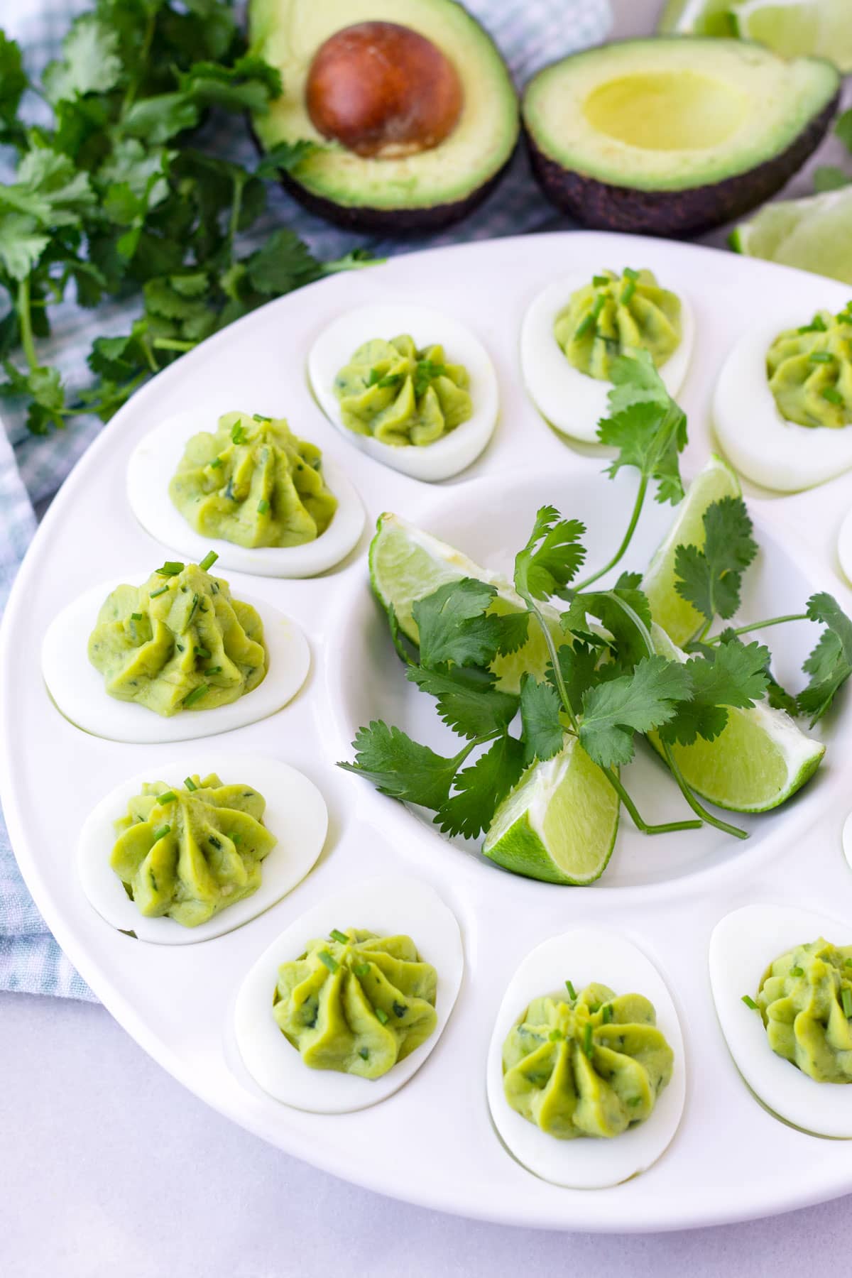 arranged avocado deviled eggs in a round plate with lime wedges and cilantro in the center