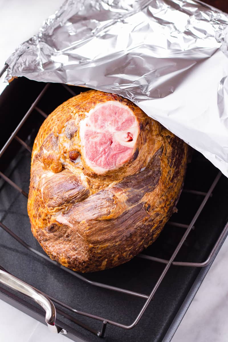a smoked half ham on a roasting rack half covered with aluminum foil