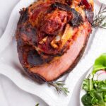 a whole cooked ham on a rectangular plate with side dishes next to it