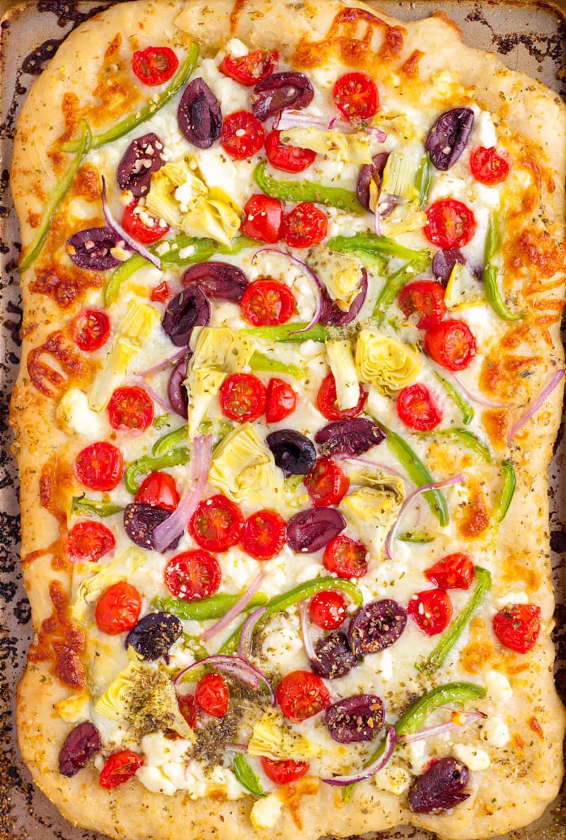 Top view of homemade colorful pizza made with olives, green bell peppers, tomatoes, artichokes, onions, and cheese
