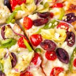 close up of pizza with olives, tomatoes, peppers, artichokes, and feta