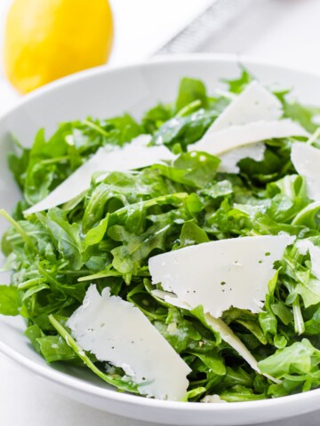 round bowl with arugula salad tossed with lemon dressing and shaved cheese