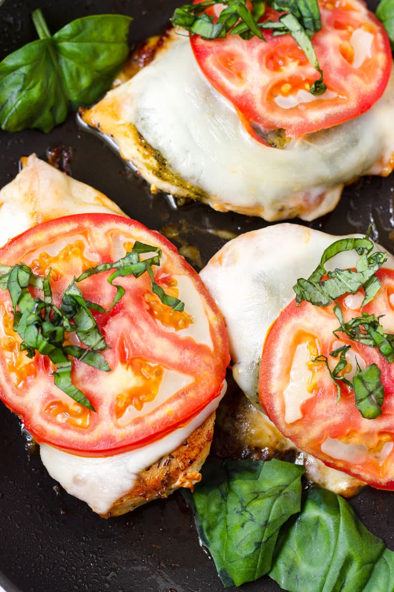 close up of seared chicken with pesto topped with cheese, tomato, and basil