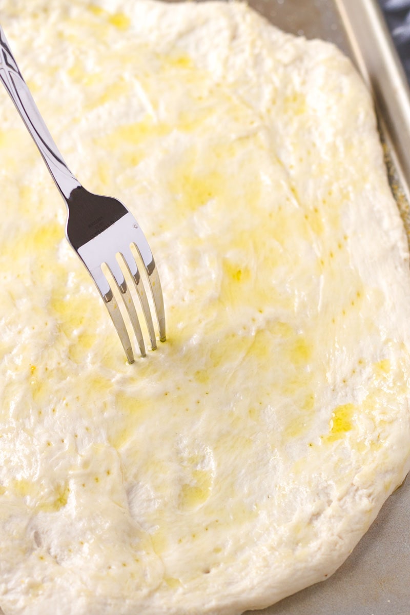 a fork pricking pizza dough that is brushed with oil