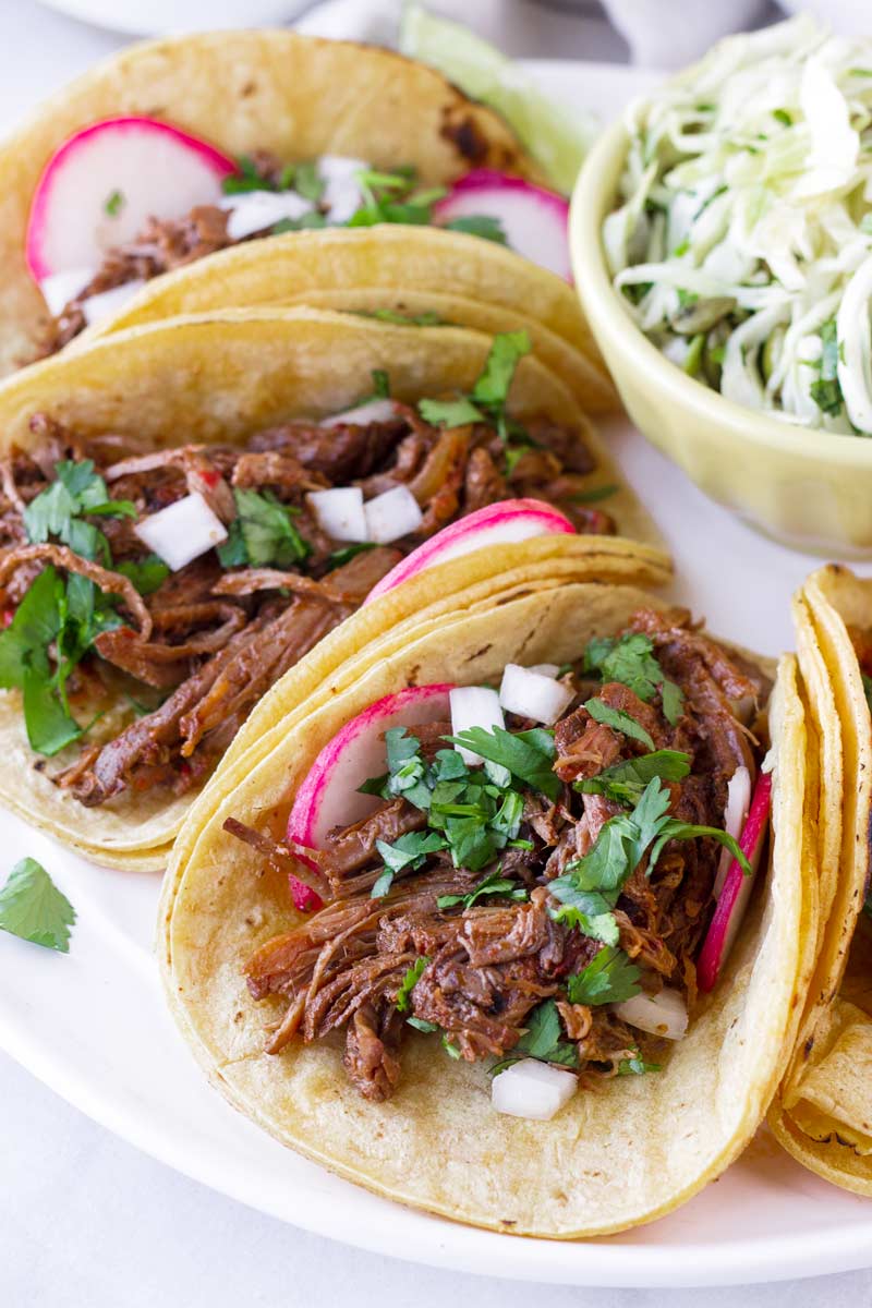 beef barbacoa tacos tucked next to each other on a plate