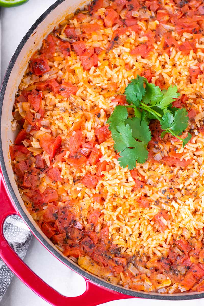 tender rice with cooked diced tomatoes on top and cilantro garnish in a pot