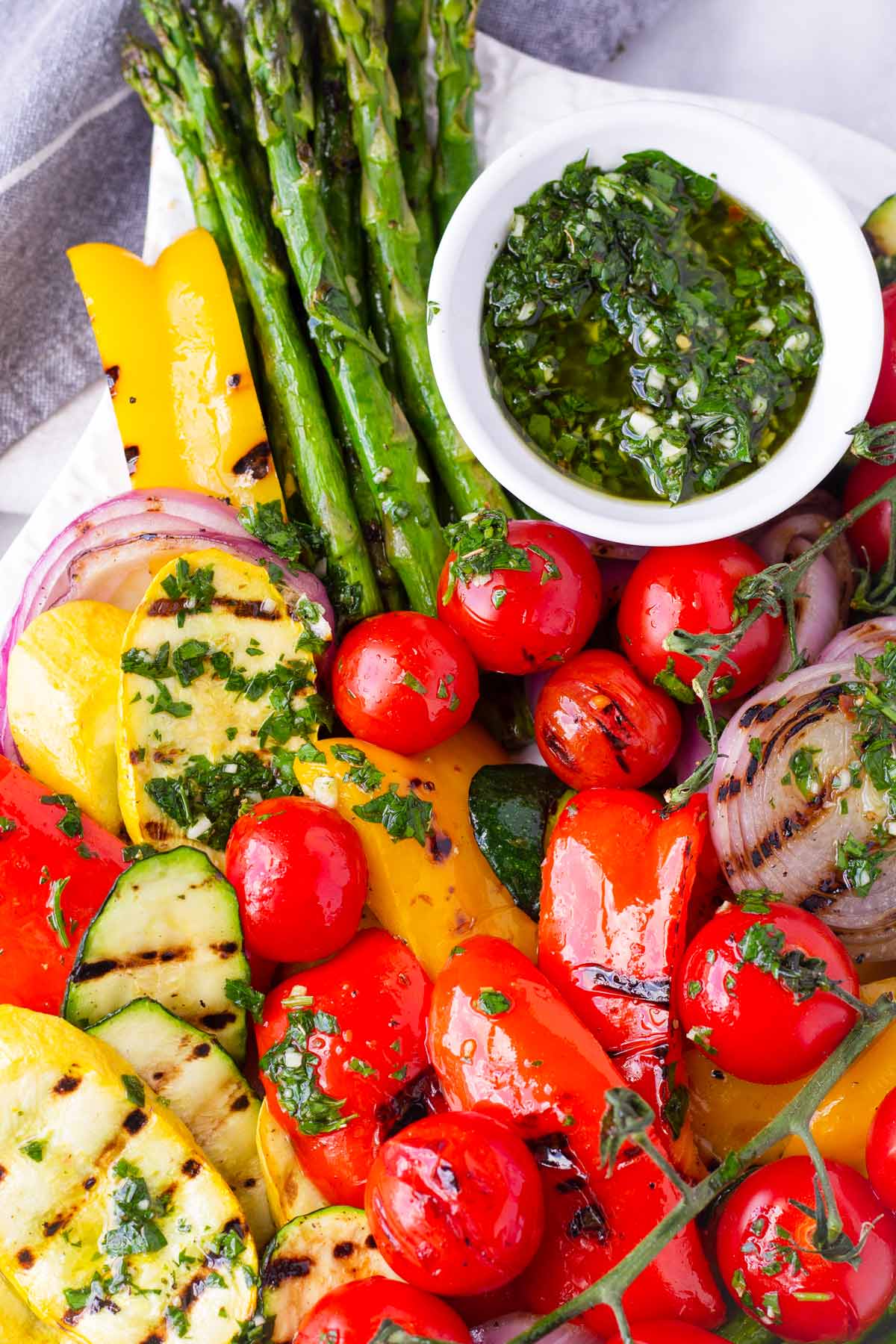 grilled summer vegetables stacked on top of each other, with a side of chimichurri sauce