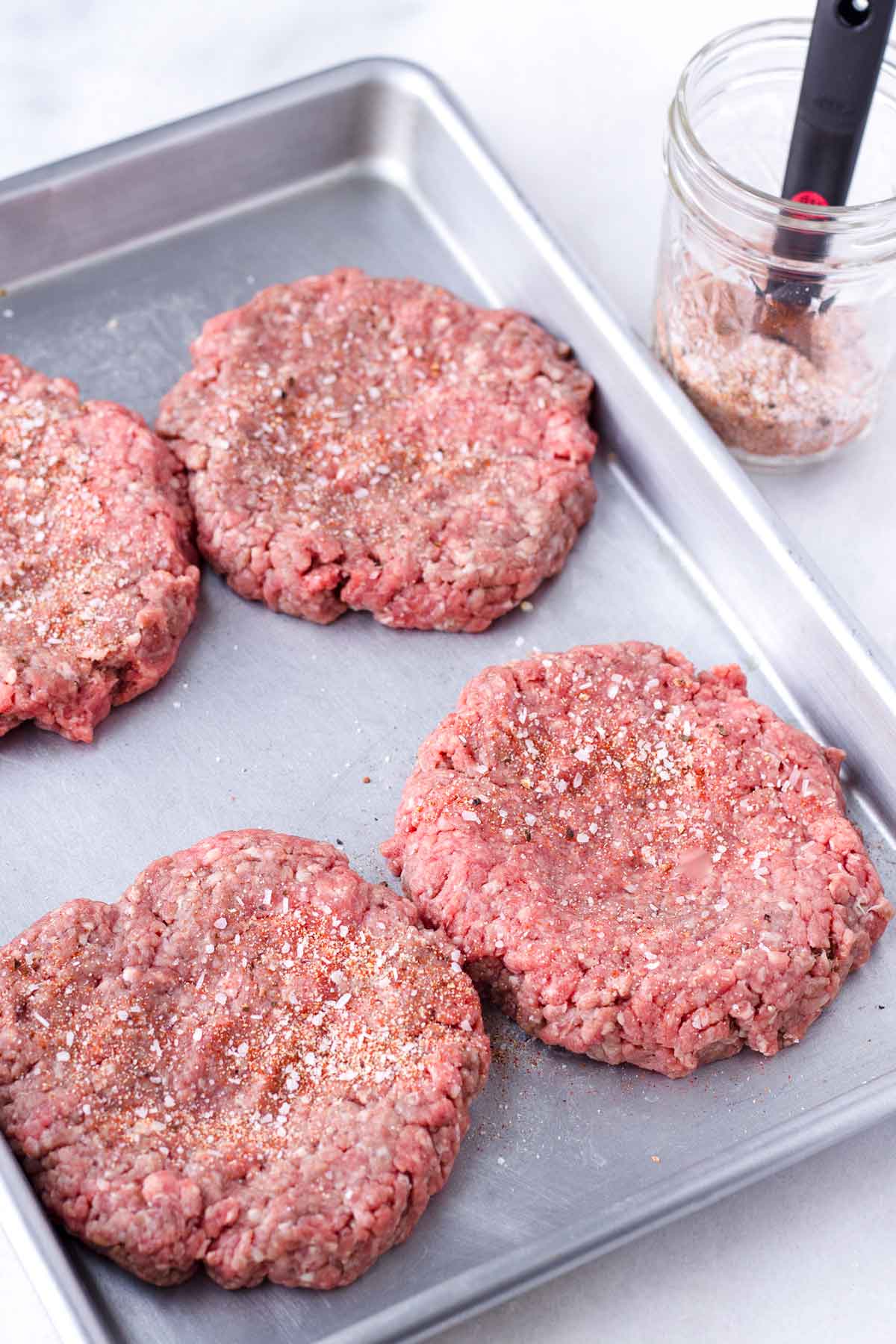 for raw beef patties with a seasoning blend on a sheet pan