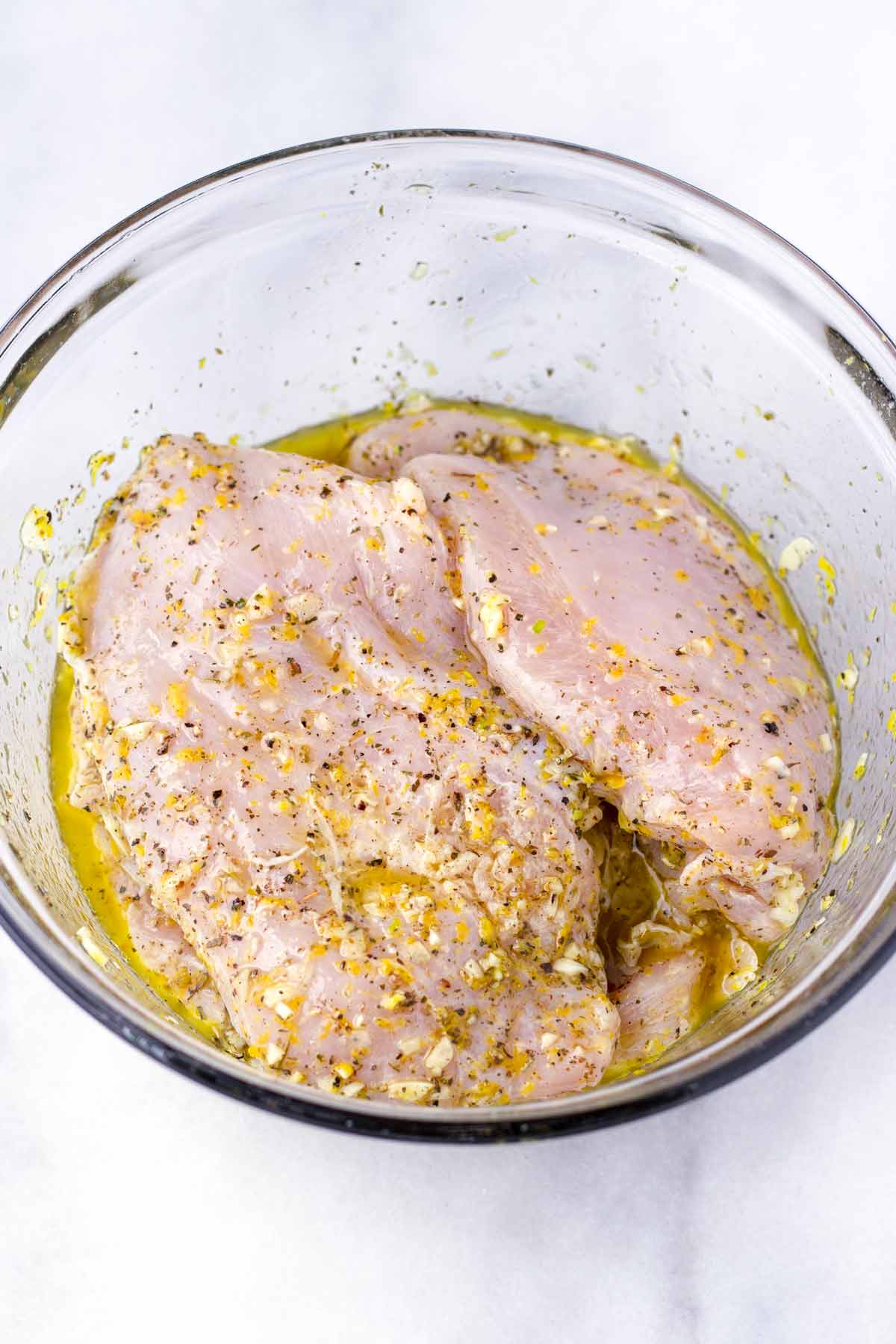 raw chicken breasts sitting in a lemon garlic marinade in a glass bowl