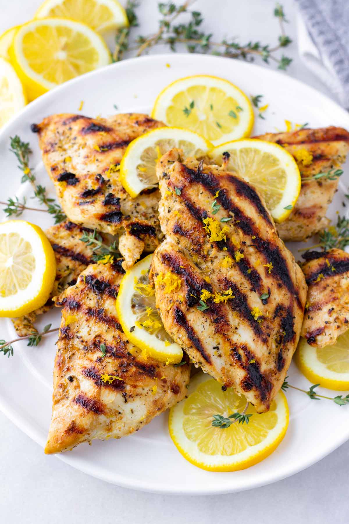 grilled lemon marinade chicken breasts arranged on a plate with lemon and thyme