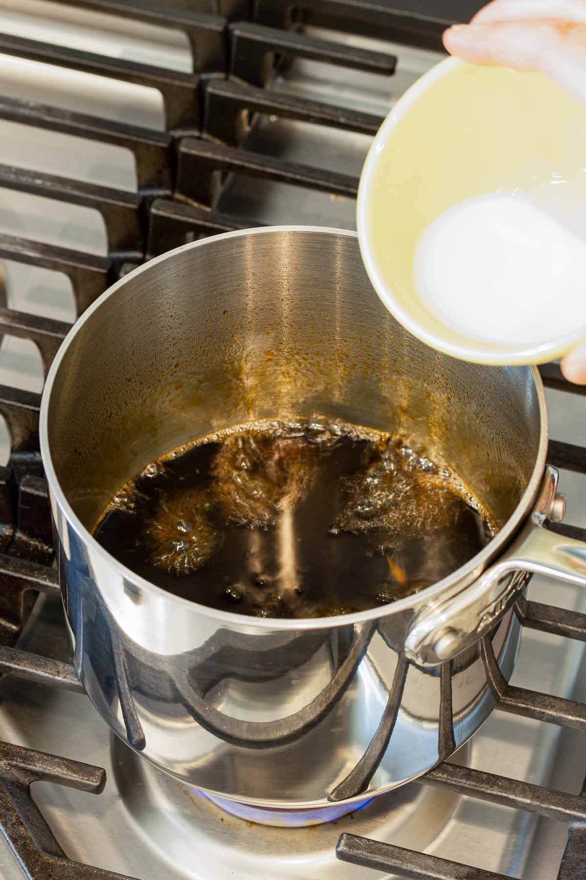 cornstarch slurry being poured into simmering sauce