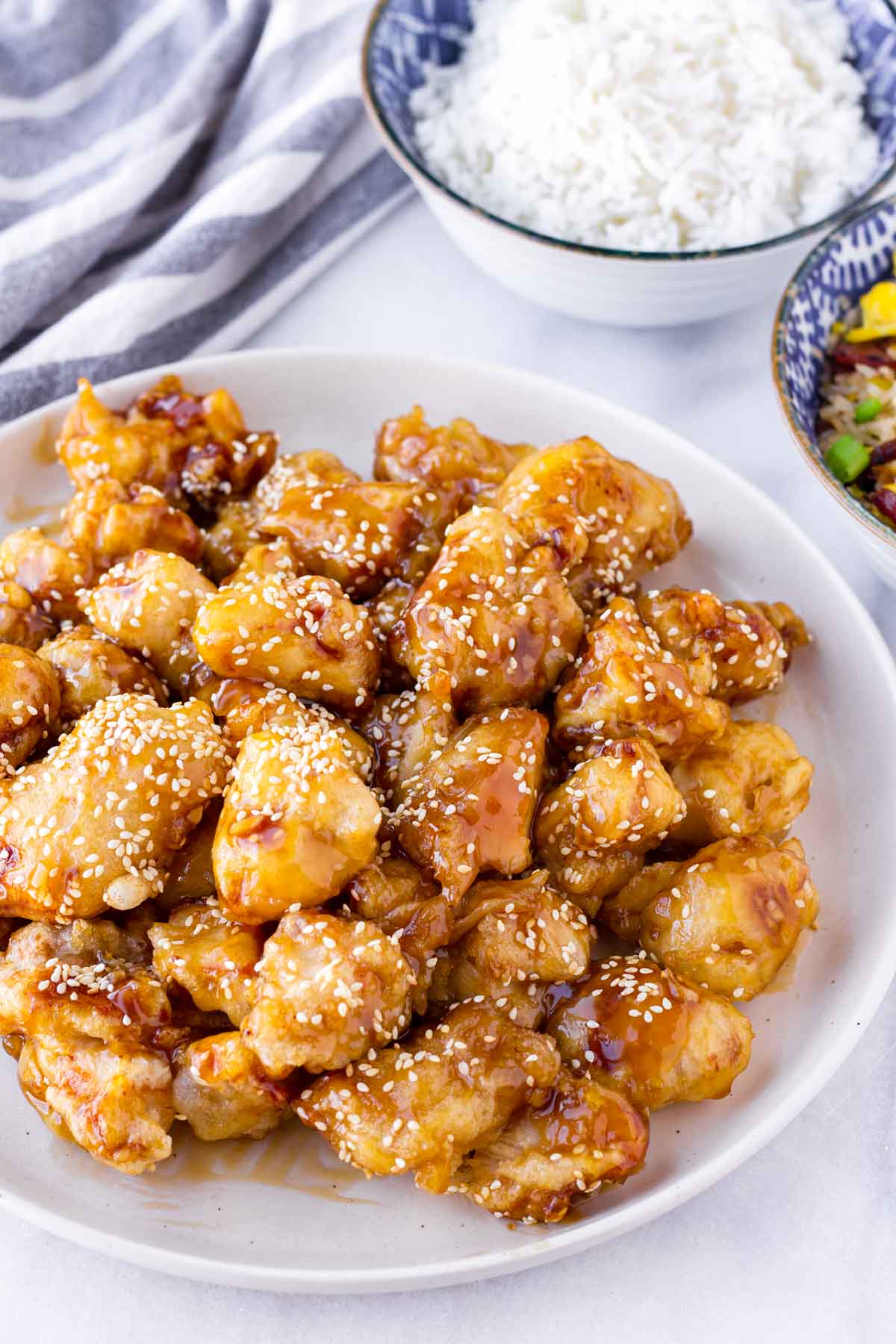 crispy honey sesame chicken on plate with two bowls of rice