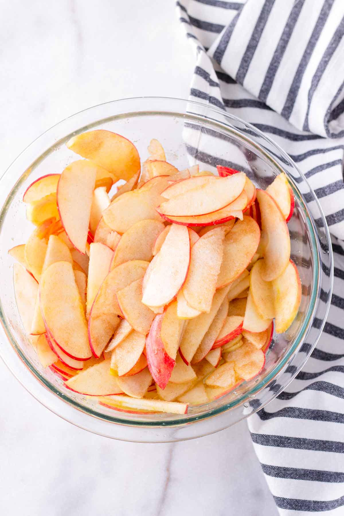 thinly sliced apples tossed with sugar and lemon juice in glass bowl