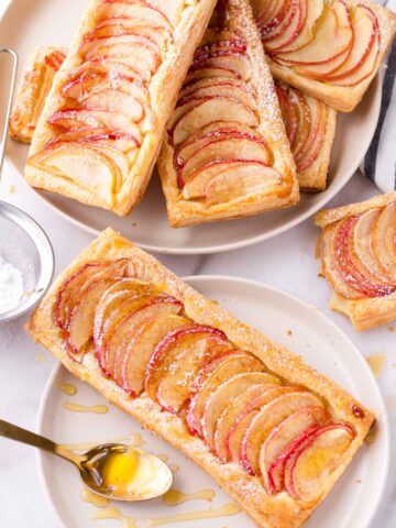 a baked puff pastry apple tart on plate with honey drizzles and a stack of more tarts
