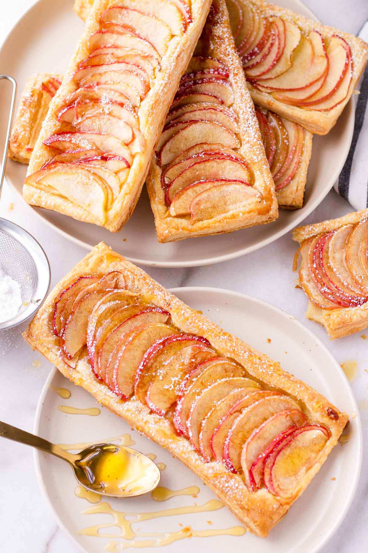 a baked puff pastry apple tart on plate with honey drizzles and a stack of more tarts