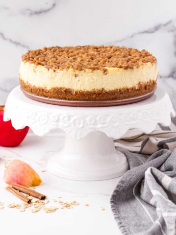 a 9 inch cheesecake topped with apples and oat crumble in a cake stand