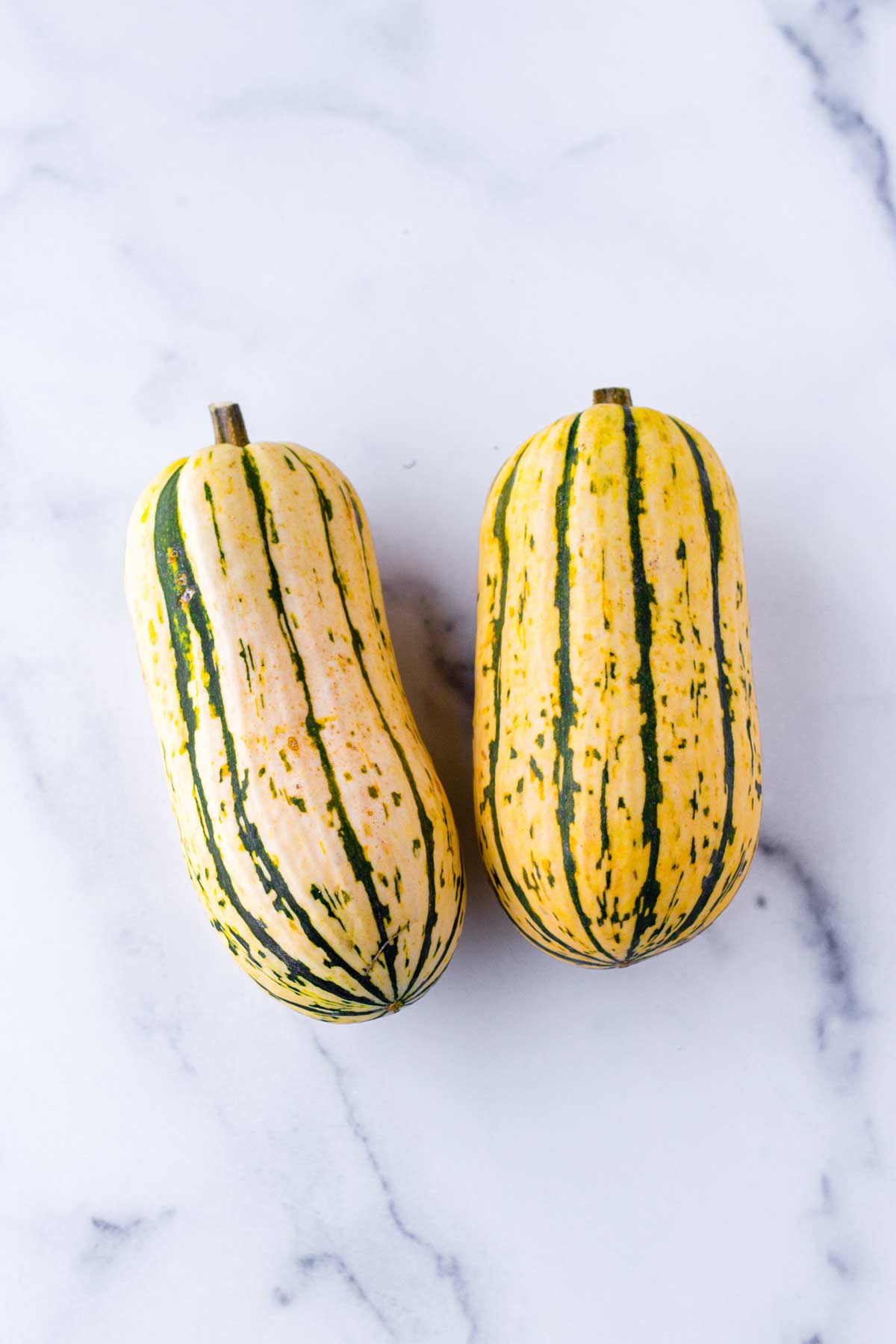 two whole unpeeled delicata squashes side by side