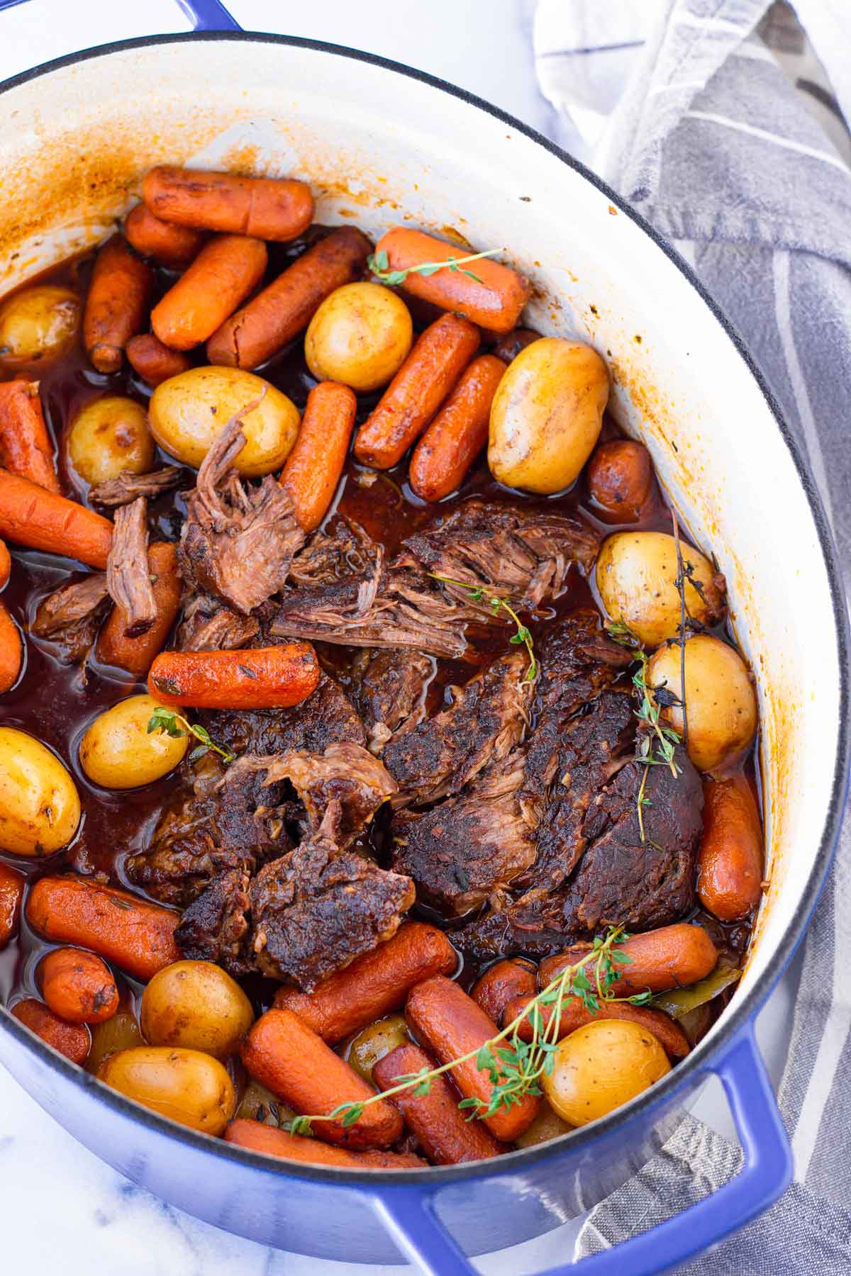 tender and roughly shredded pot roast in an oval dutch oven