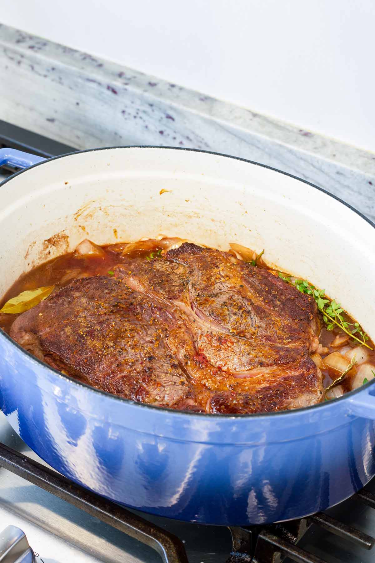 seared chuck roast in a blue oval dutch oven