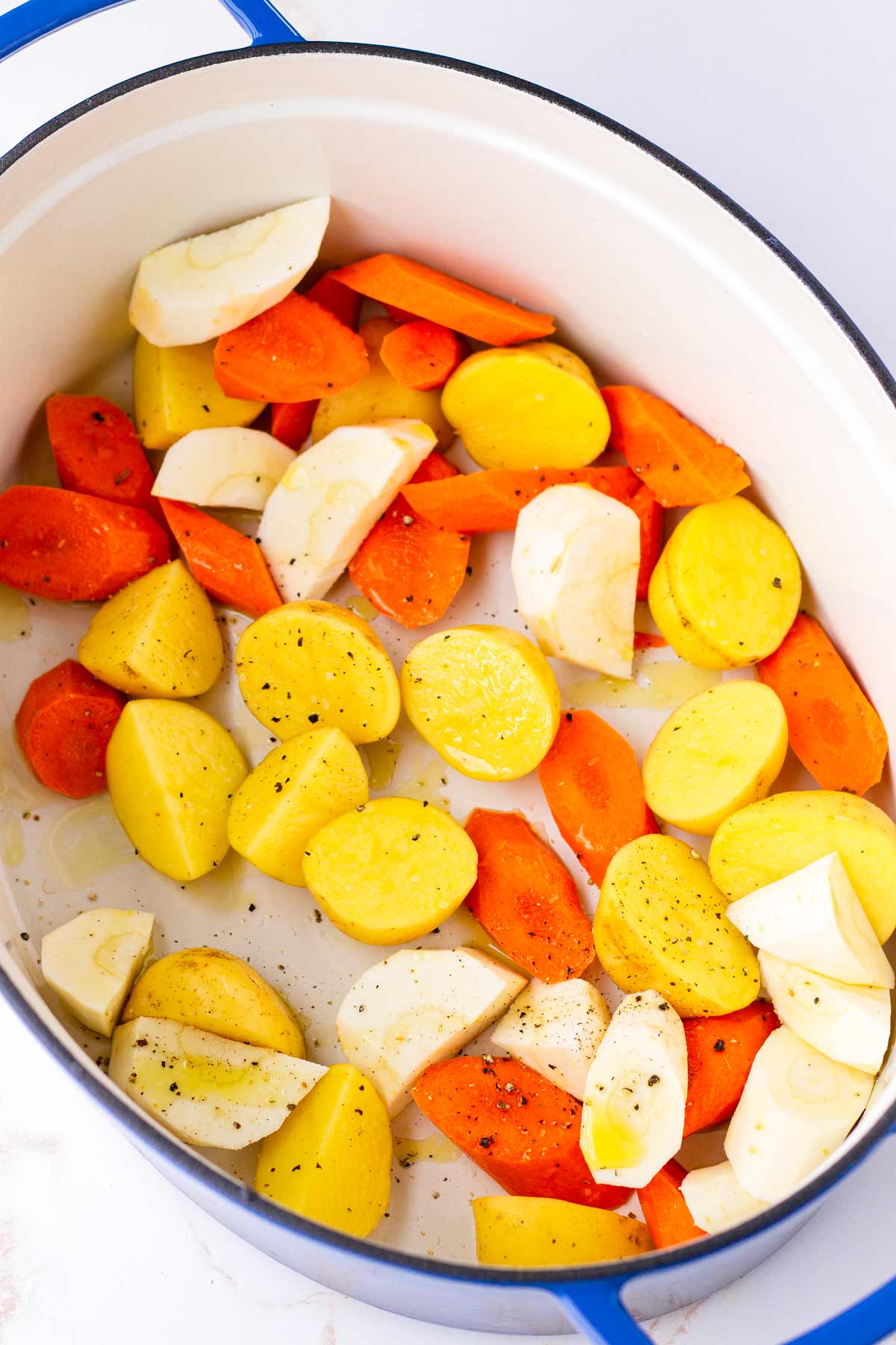 a bed of potatoes, parsnips, and carrots inside a blue dutch oven