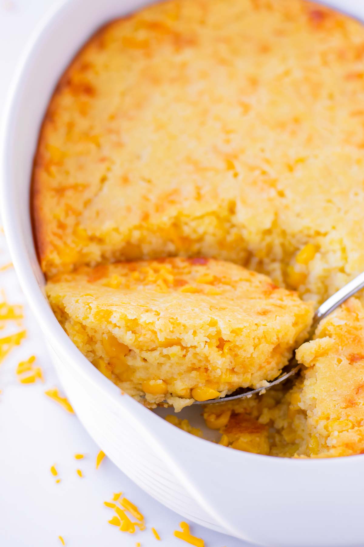 a spoon scooping out a serving of corn casserole from pan