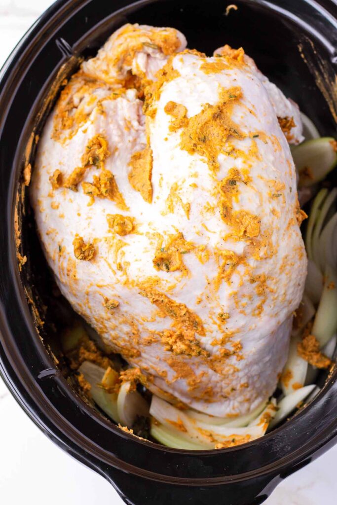 uncooked turkey breast rubbed with spiced butter in a slow cooker