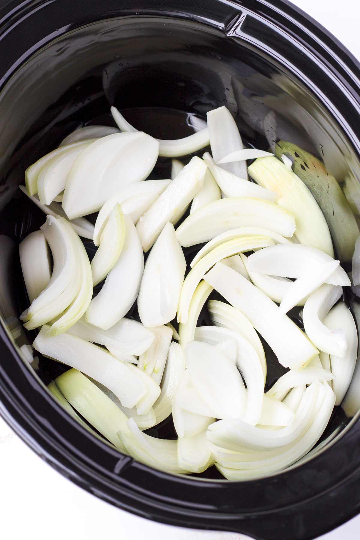 sliced raw onions in a large oval shaped slow cooker