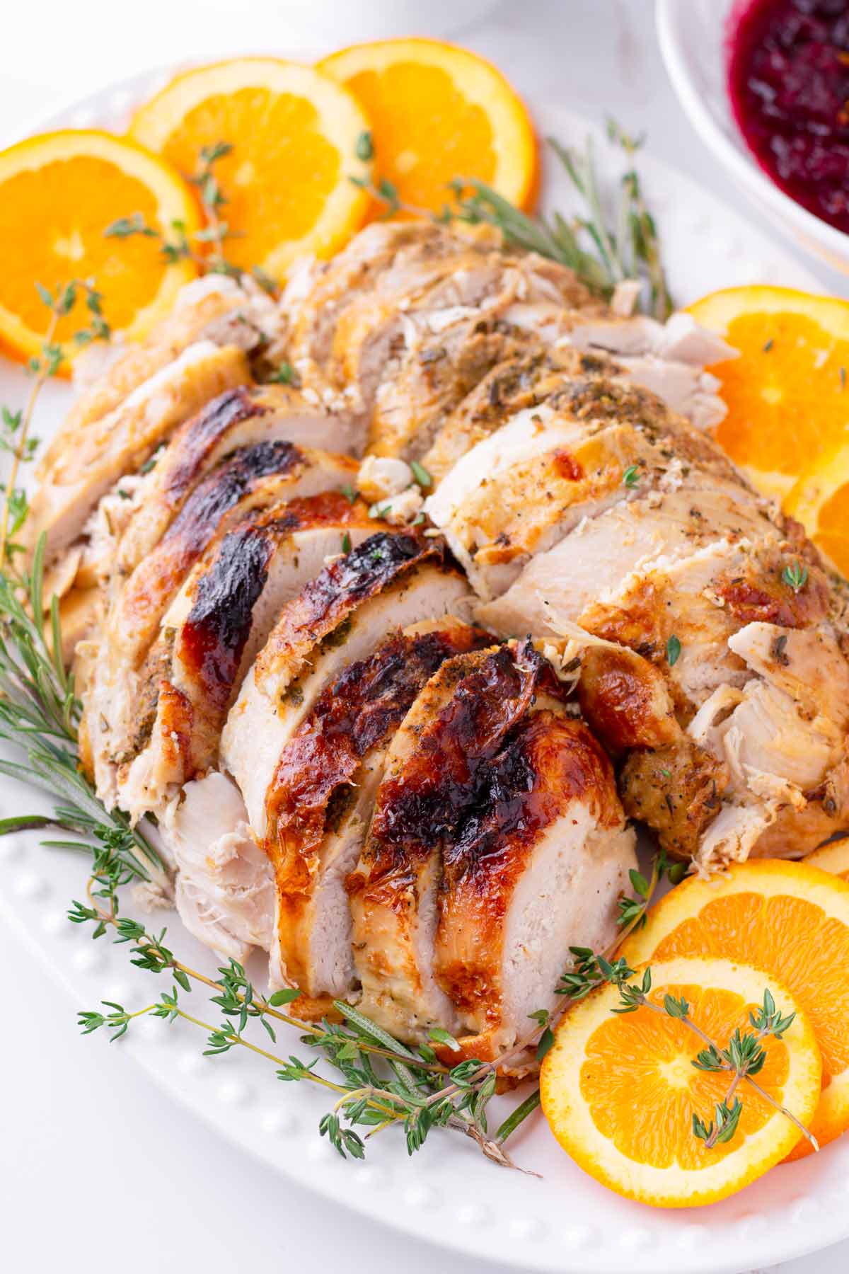 oval platter with sliced turkey breast and herb and orange decorations