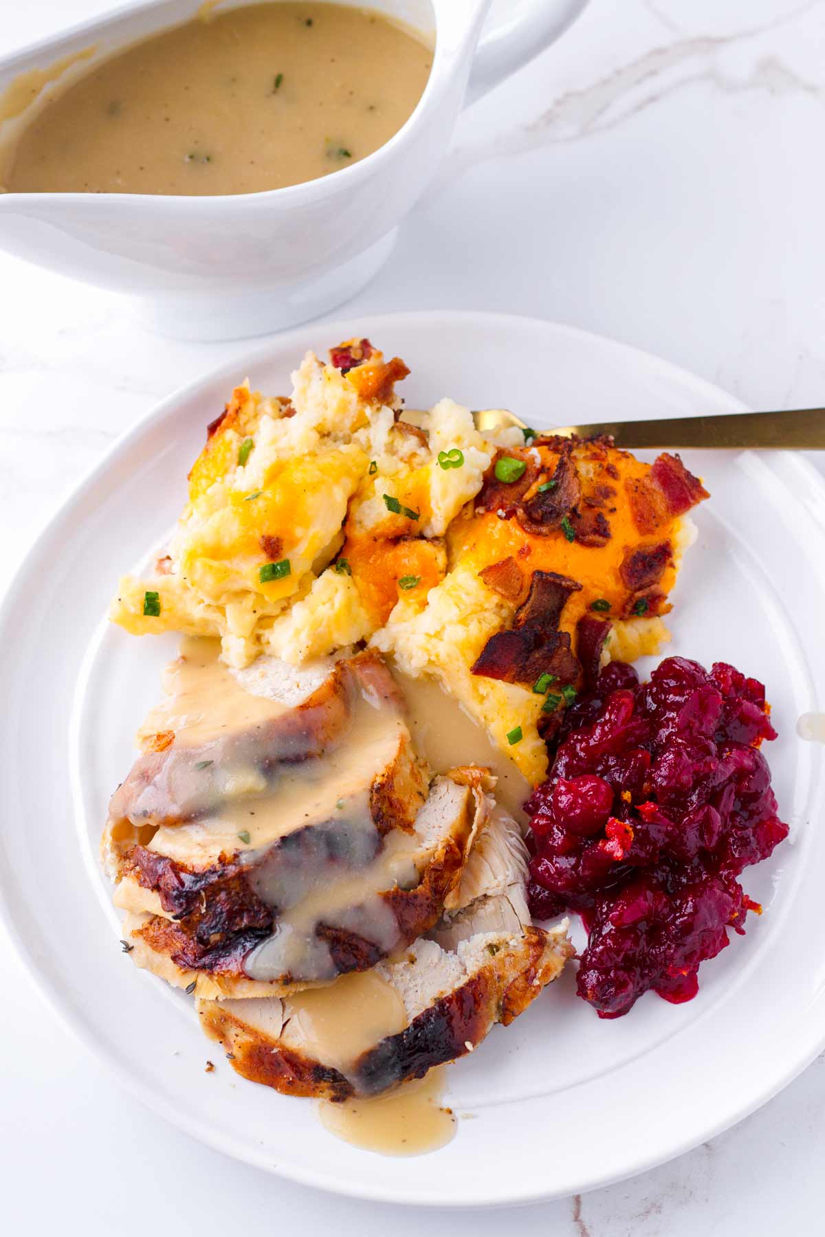 a plate of turkey breast slices with gravy on top next to cranberry and potatoes