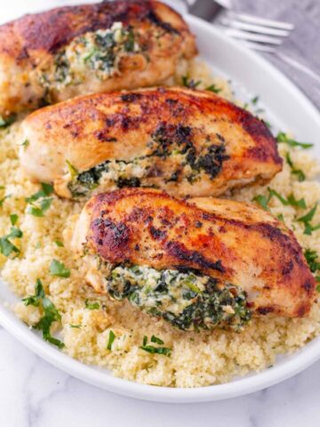 three pieces of spinach and cheese chicken breasts on top of couscous