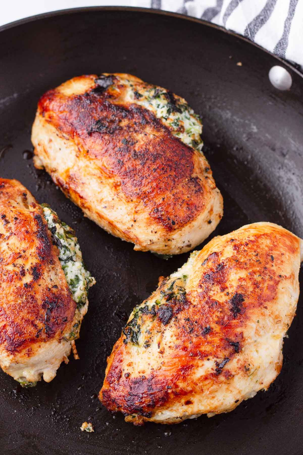 golden brown pan-seared stuffed chicken breasts on nonstick skillet
