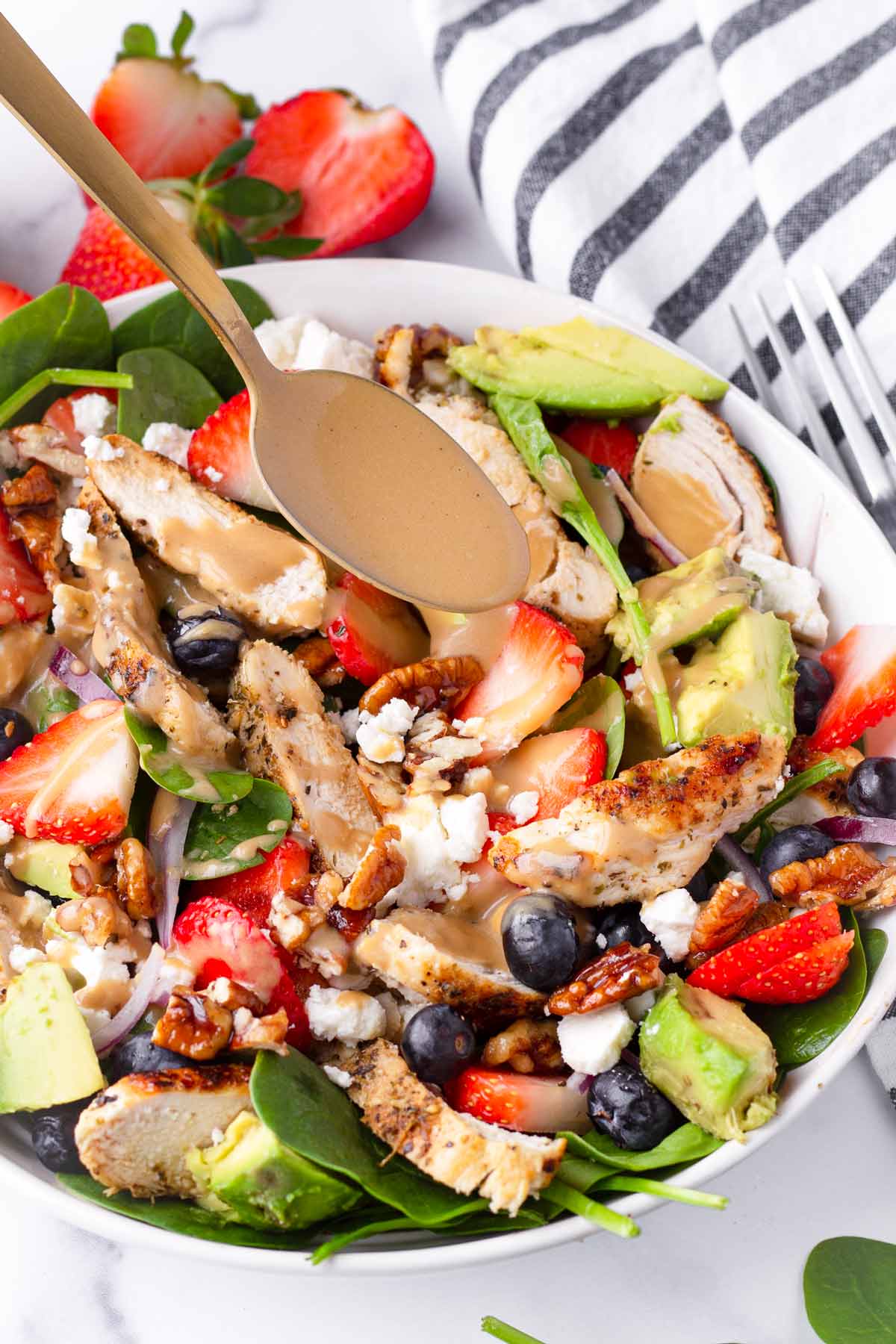 drizzling creamy balsamic dressing over spinach chicken salad bowl