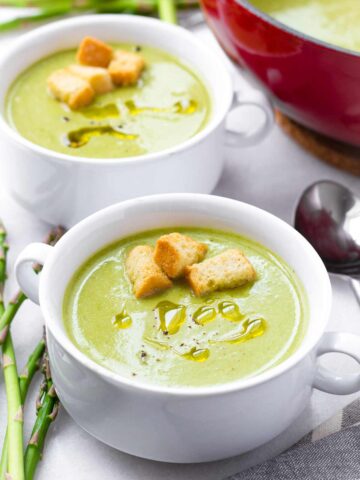 two bowls of cream of asparagus with olive oil drizzle and croutons