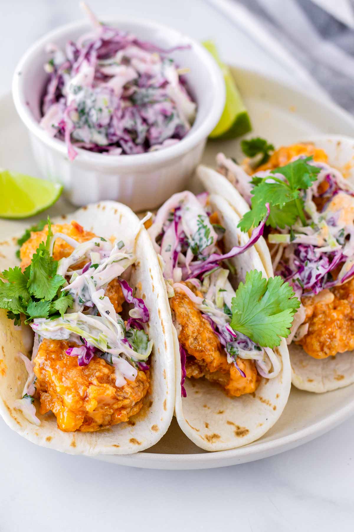 three folded tacos served on a plate with a side of slaw
