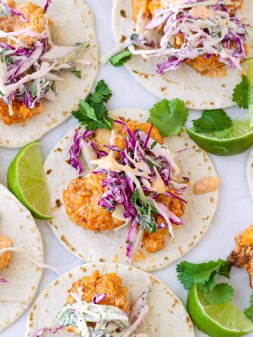 five open faced bang bang shrimp tacos topped with coleslaw and lime garnish