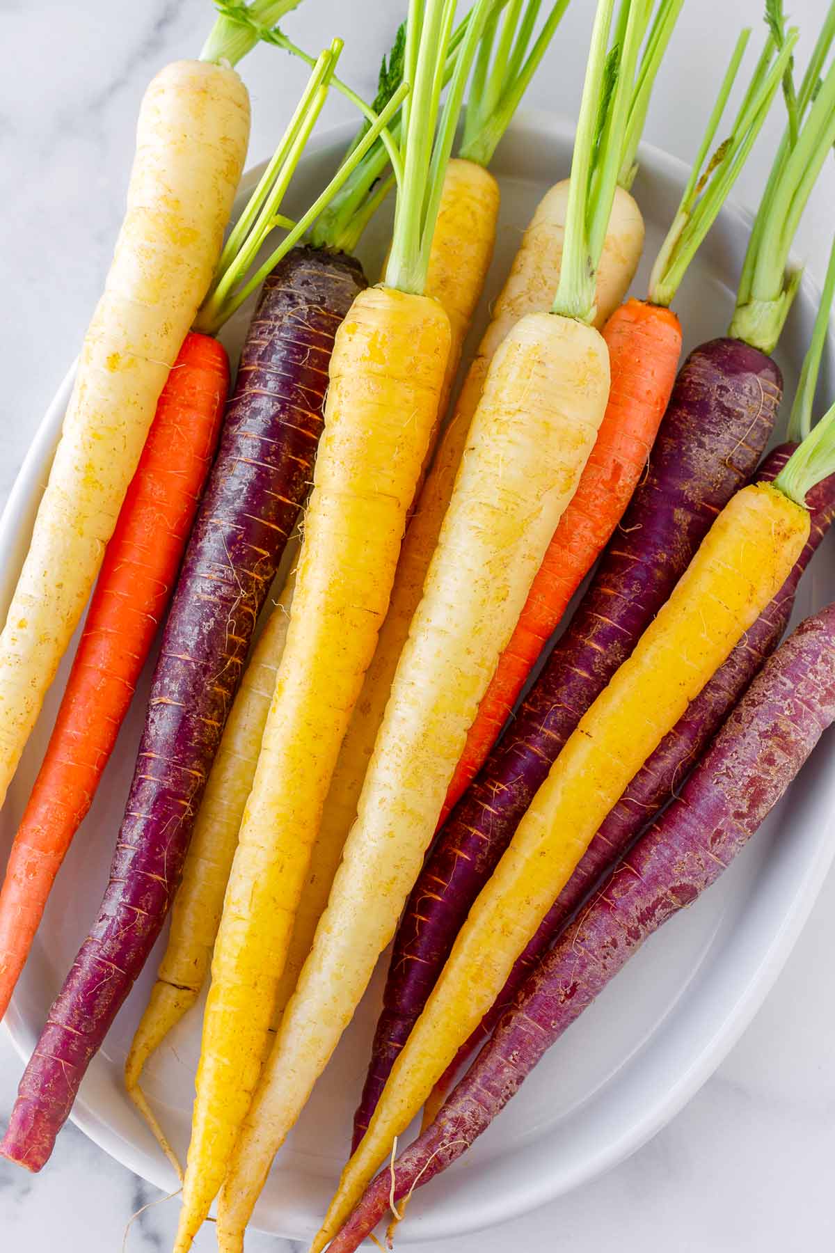 raw uncooked multicolor carrots arranged on an oval plate