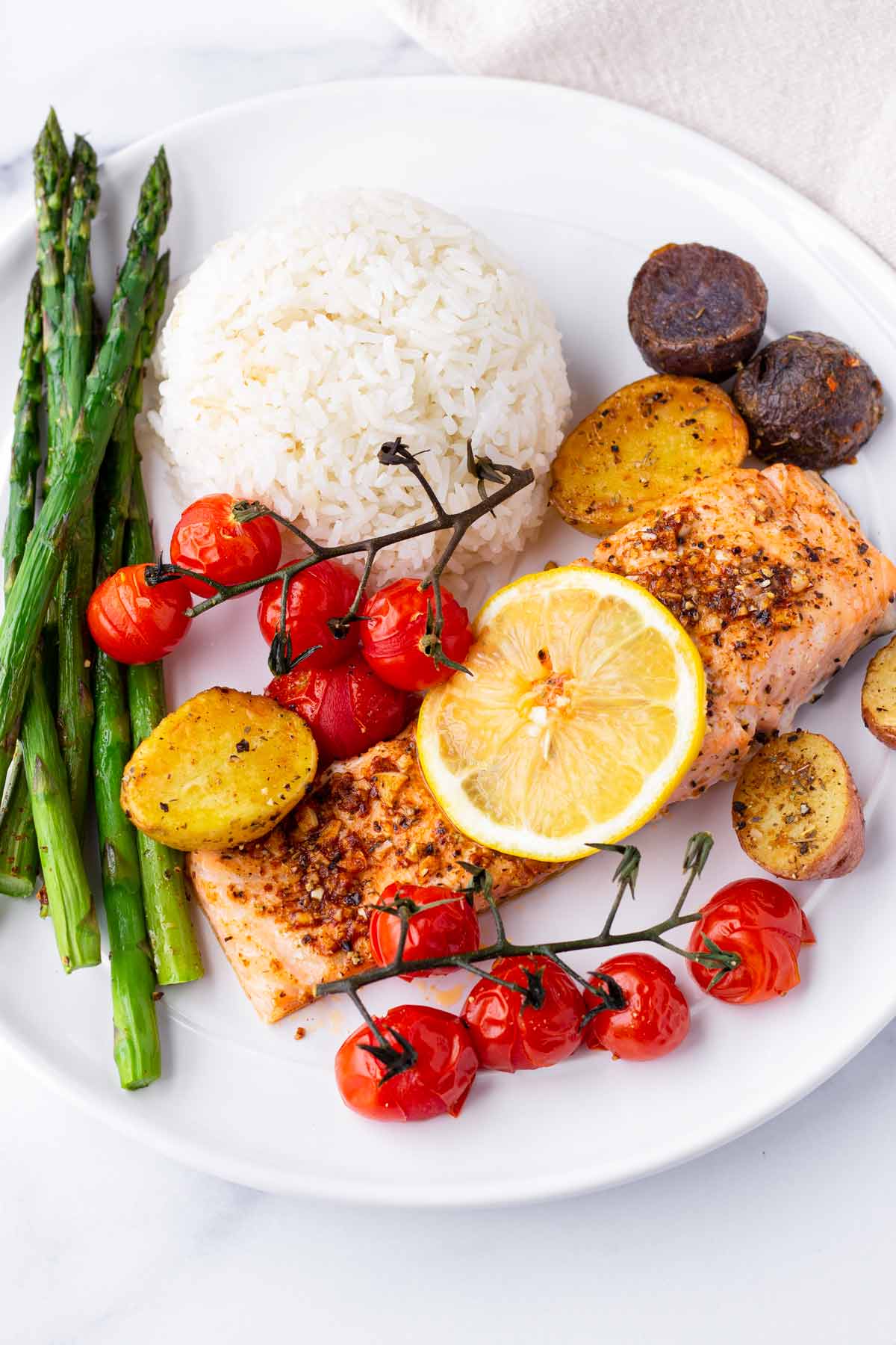 a plate with asparagus, tomatoes, potatoes, salmon, and rice