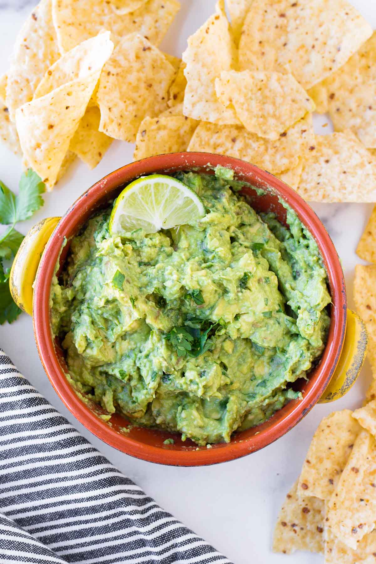 4 ingredient guac in an orange and yellow bowl and a spread of tortilla chips