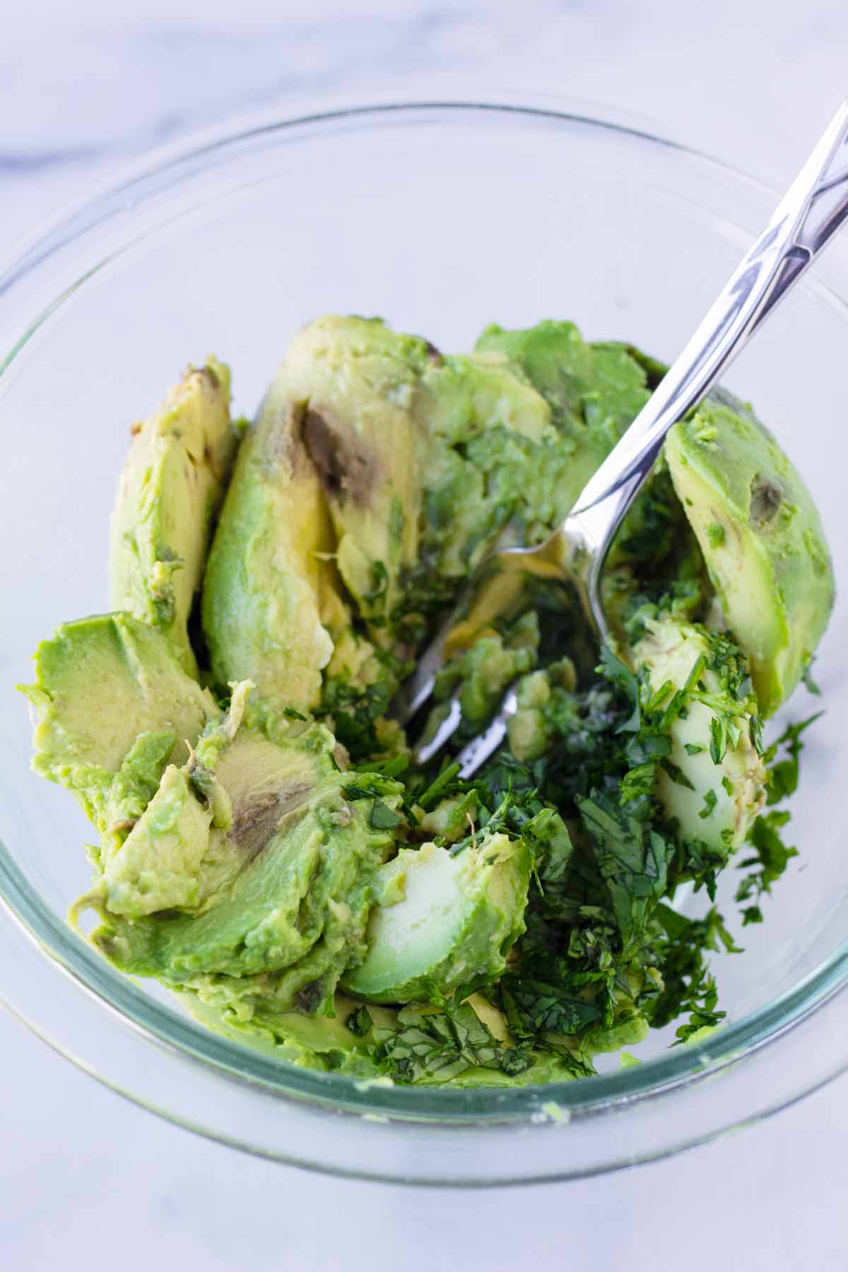 a glass bowl with unmashed avocado chunks, cilantro, lime juice, and salt