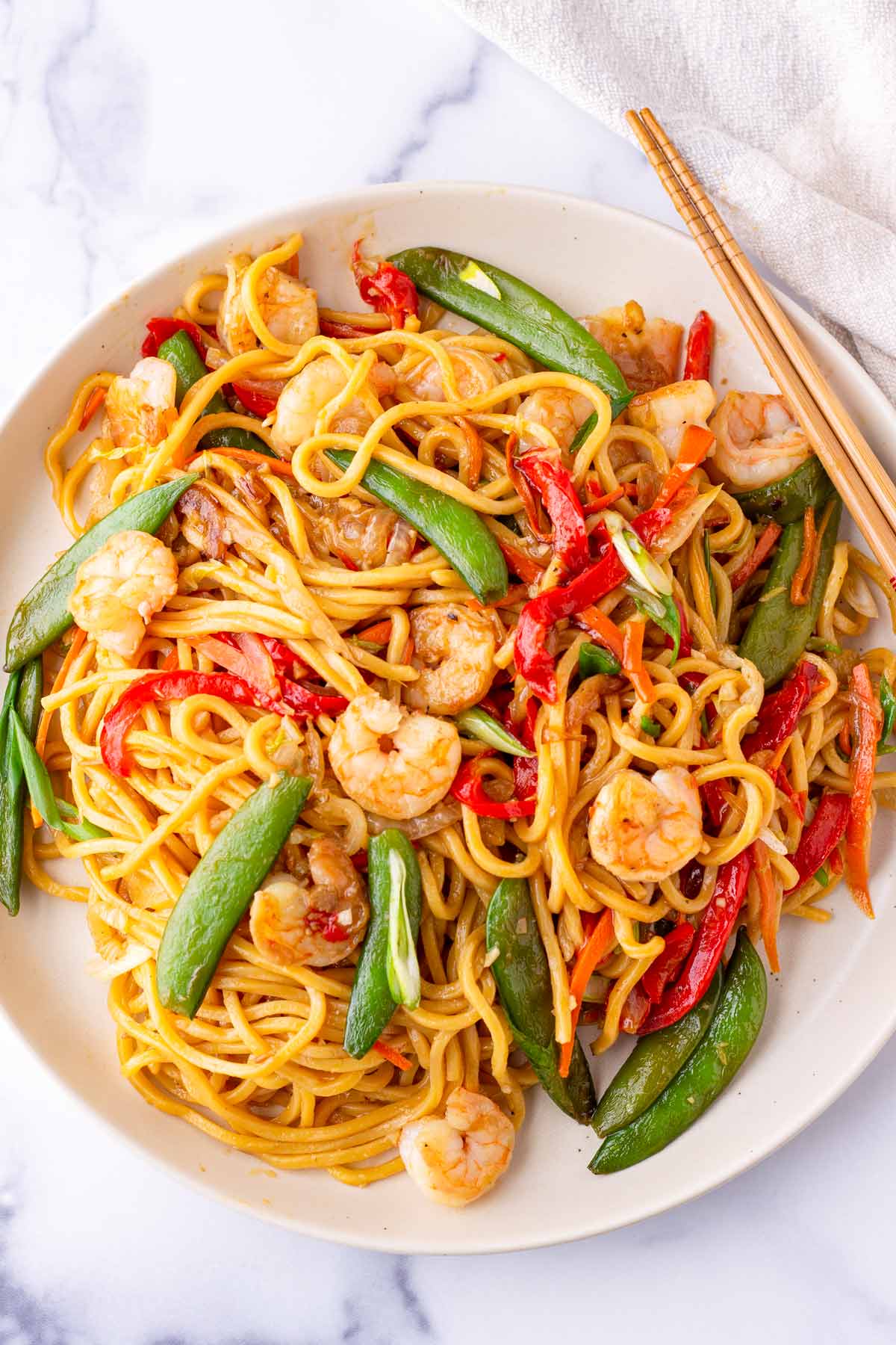 a plate with shrimp lo mein noodles with snap peas, bell peppers, and sauce