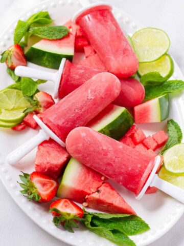 four watermelon popsicles on an oval plate with garnish