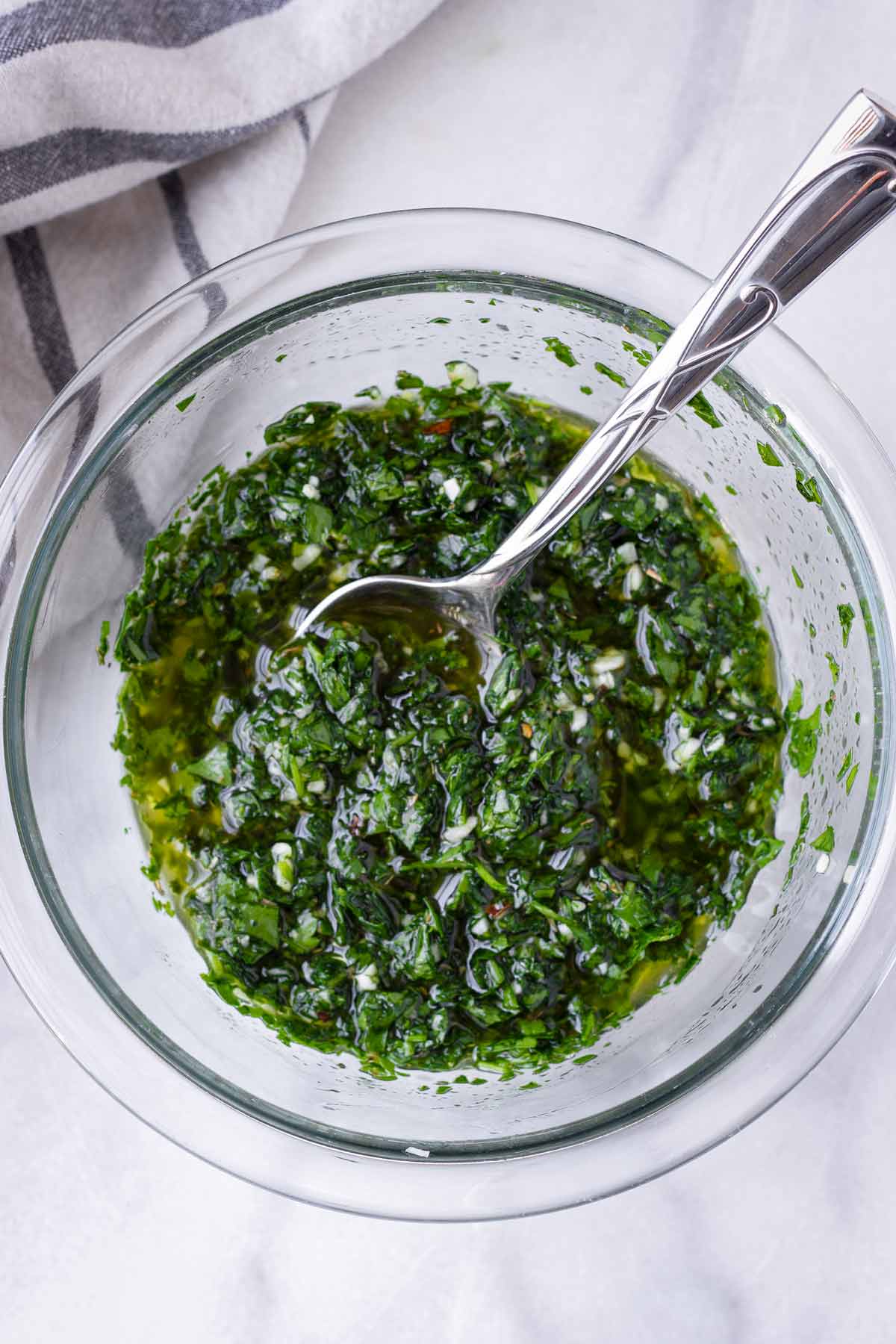 mixing chimichurri sauce in a glass bowl with a spoon
