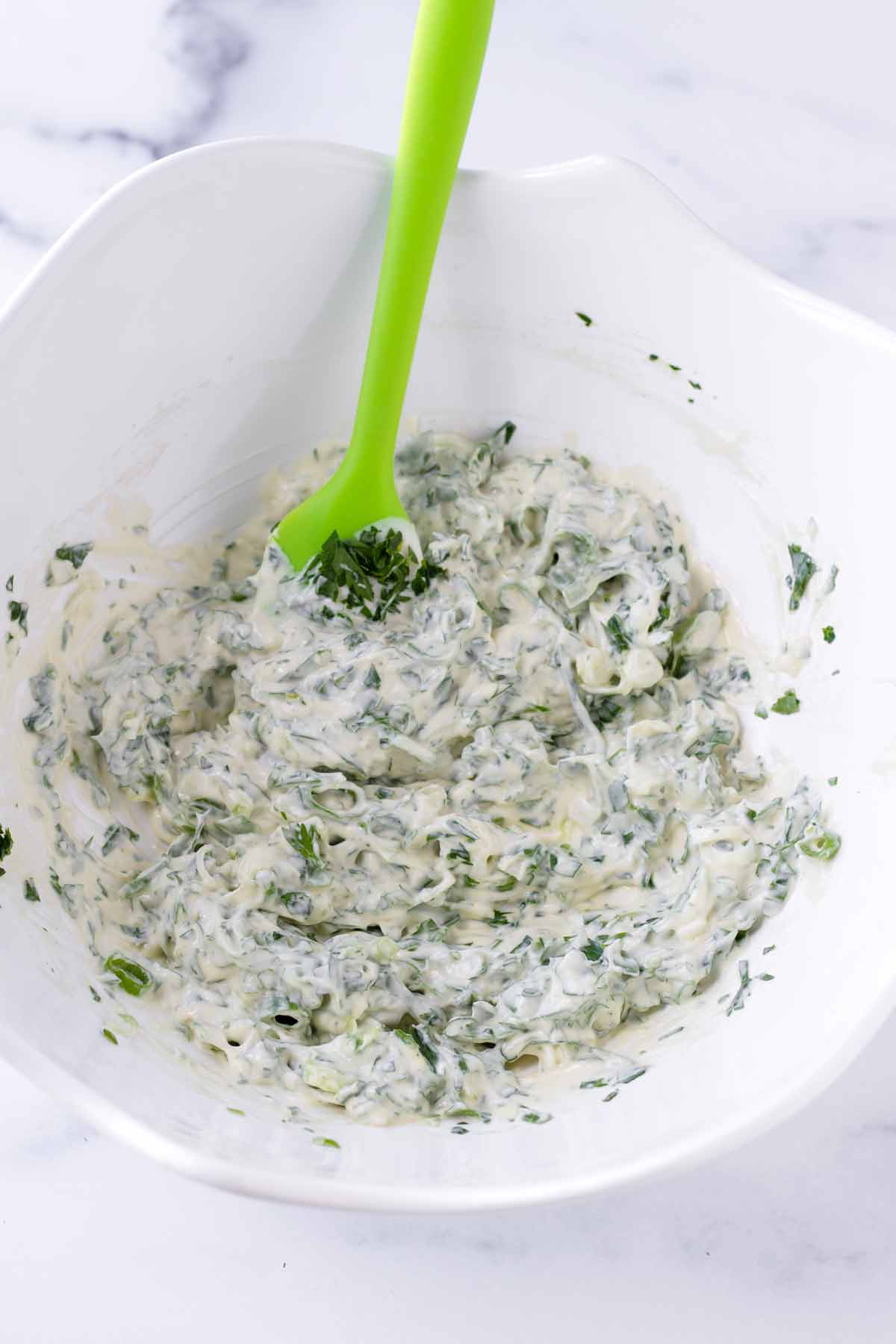 mixing the creamy mayo and herb dressing with a rubber spatula