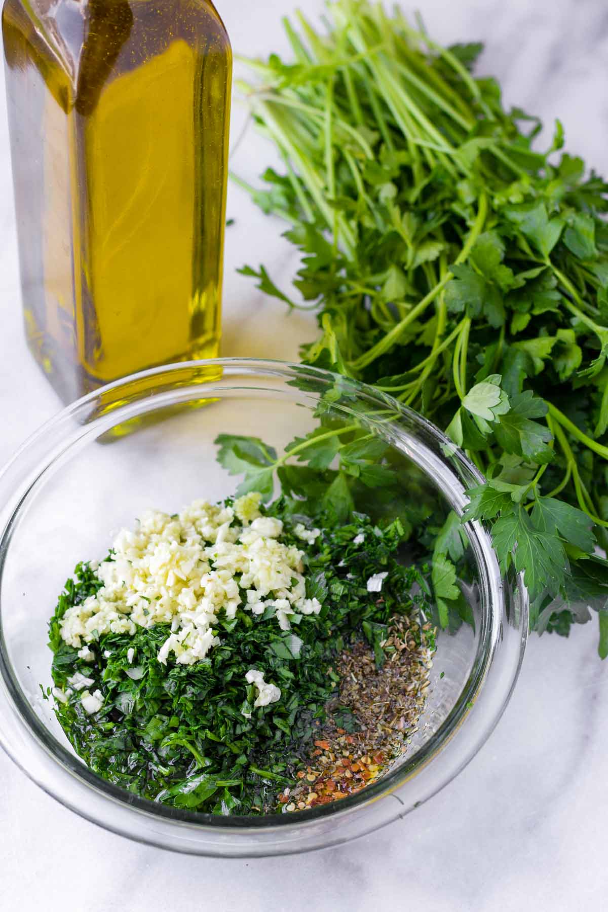 unmixed ingredients in a bowl next to parsley and a bottle of olive oil
