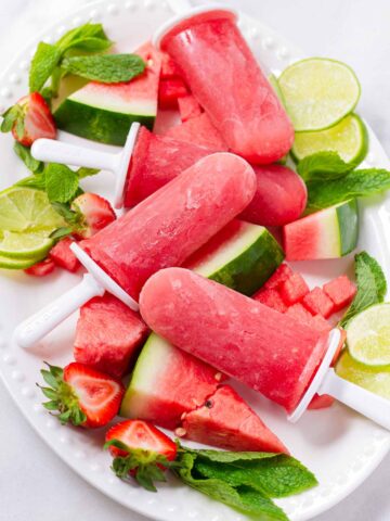 four watermelon popsicles on an oval plate with garnish