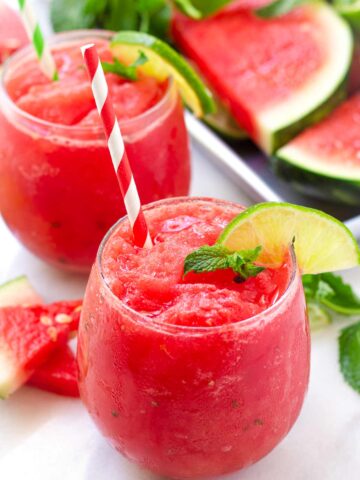 two glasses of watermelon slushies with lime garnish